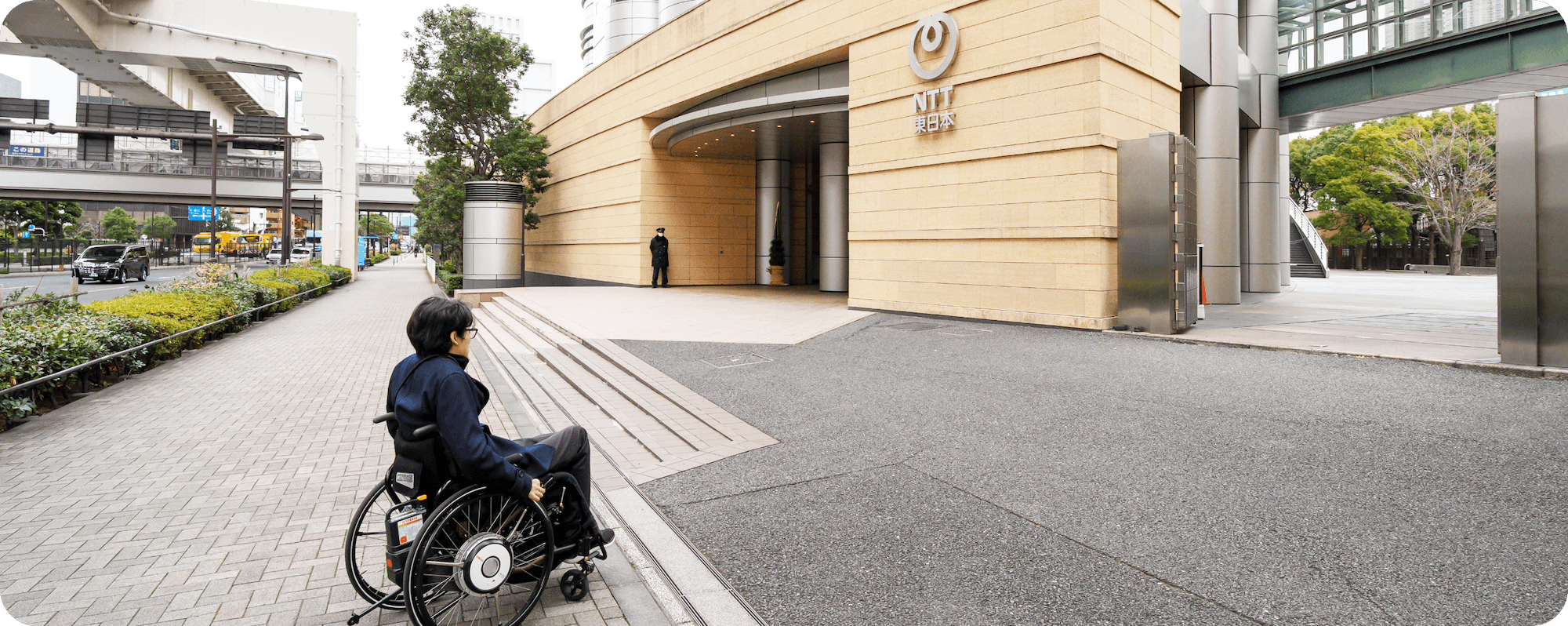 NTT東日本本社ビルの入口に向かう車いす利用者